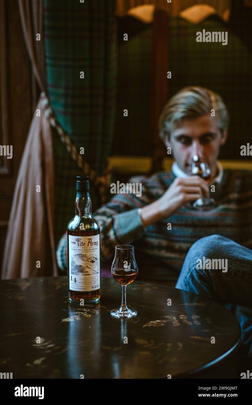 Junger Mann, der im Sessel sitzt und Single-Malt-Whisky im Glas isst. Stockfoto