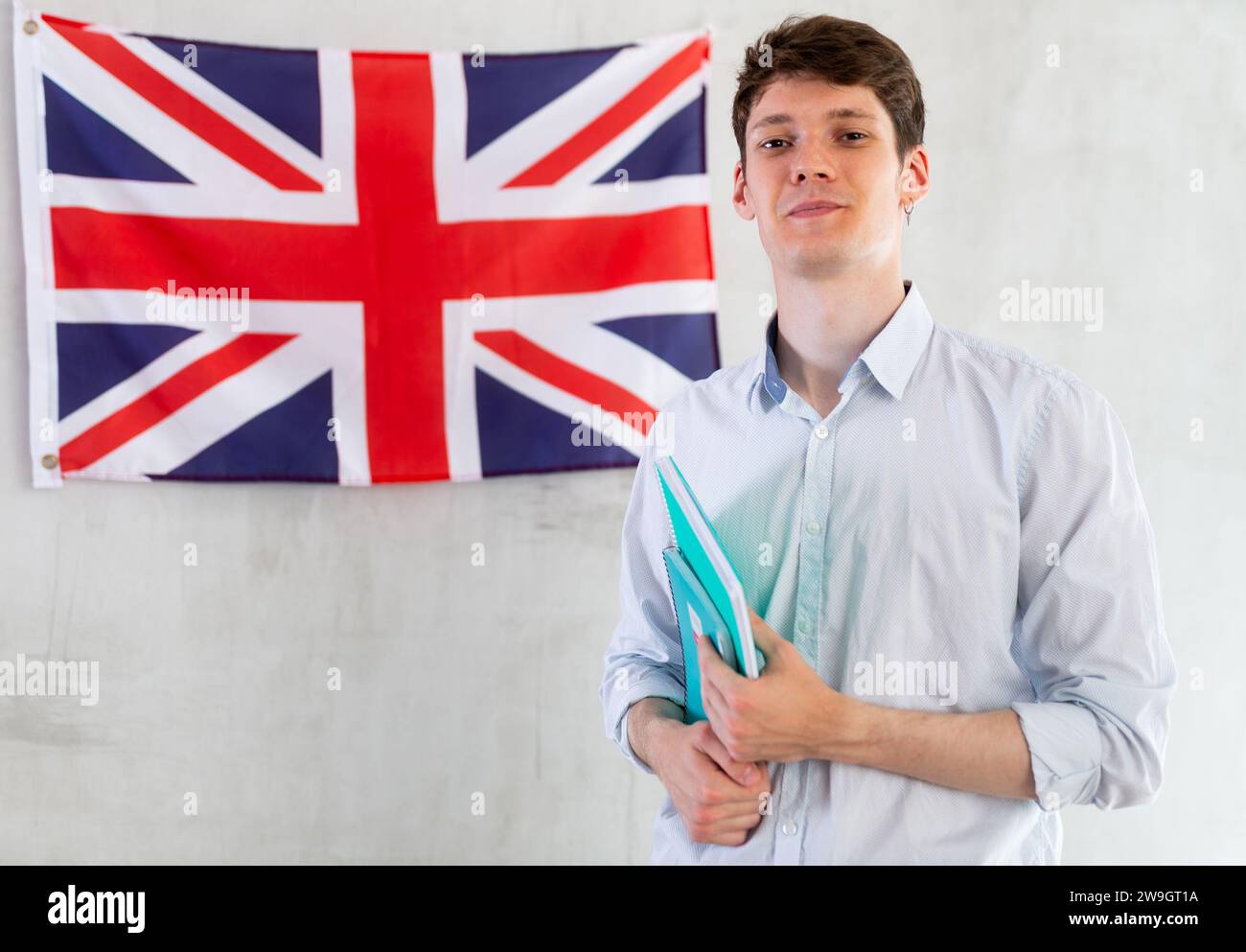 Zufriedener männlicher Student mit Notizbüchern in der Hand vor dem Hintergrund der britischen Flagge. Konzept des Auslandsstudiums und der Einwanderung Stockfoto
