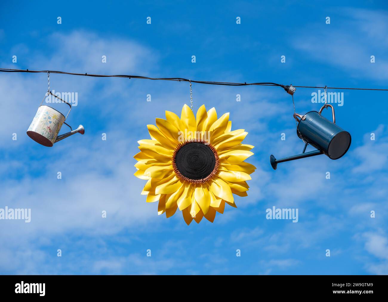 Gartendekoration mit Gießkannen und einer Sonnenblume, die unter blauem Himmel hängt Stockfoto