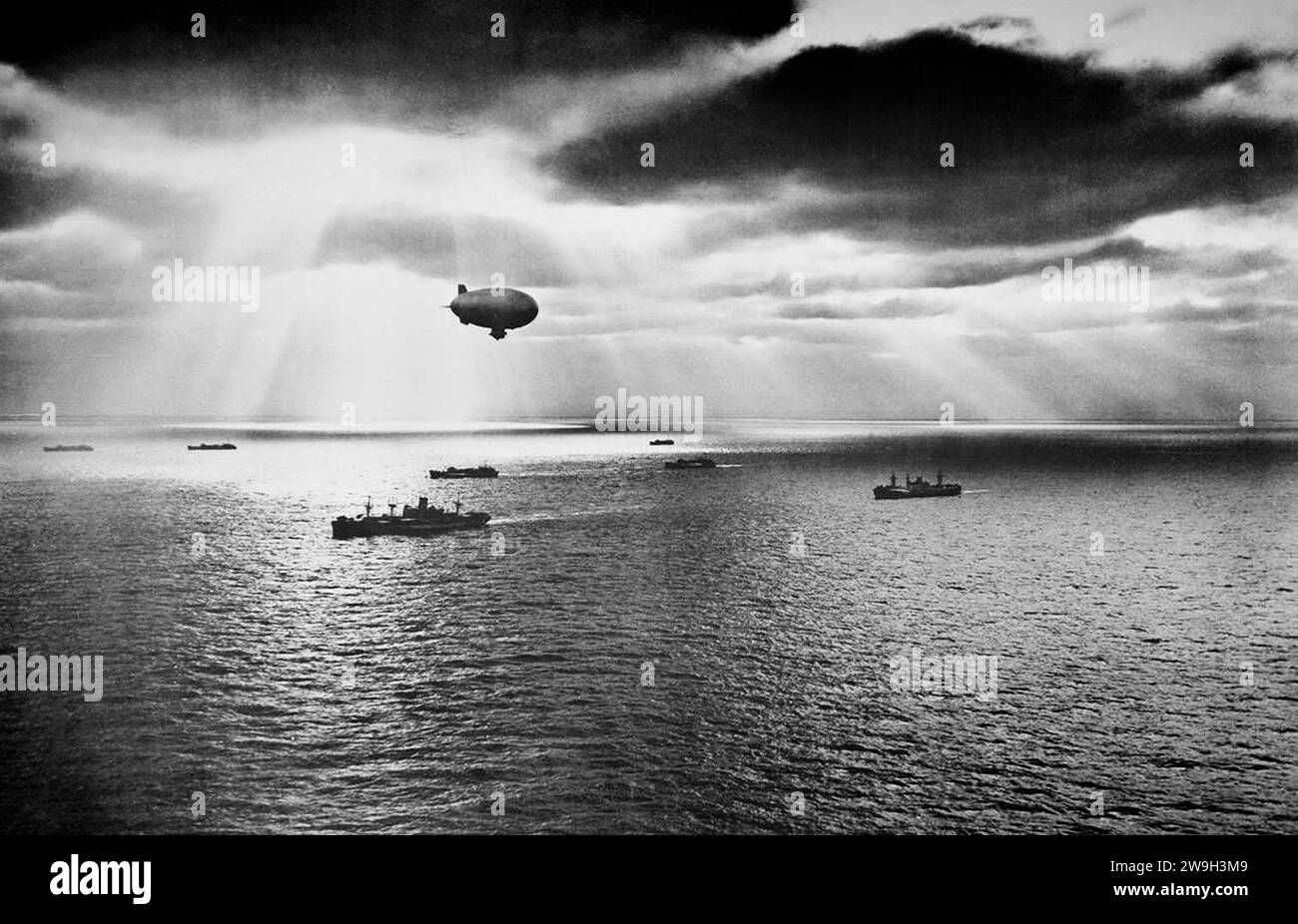 Bei Sonnenuntergang über dem Atlantik bewegt sich ein US-Konvoi während des Zweiten Weltkriegs friedlich auf ihn zu Ein Luftfeuer der US Navy, der über dem Kopf schwebt, ist im Juni 1943 auf der Suche nach Anzeichen feindlicher U-Boote. Stockfoto