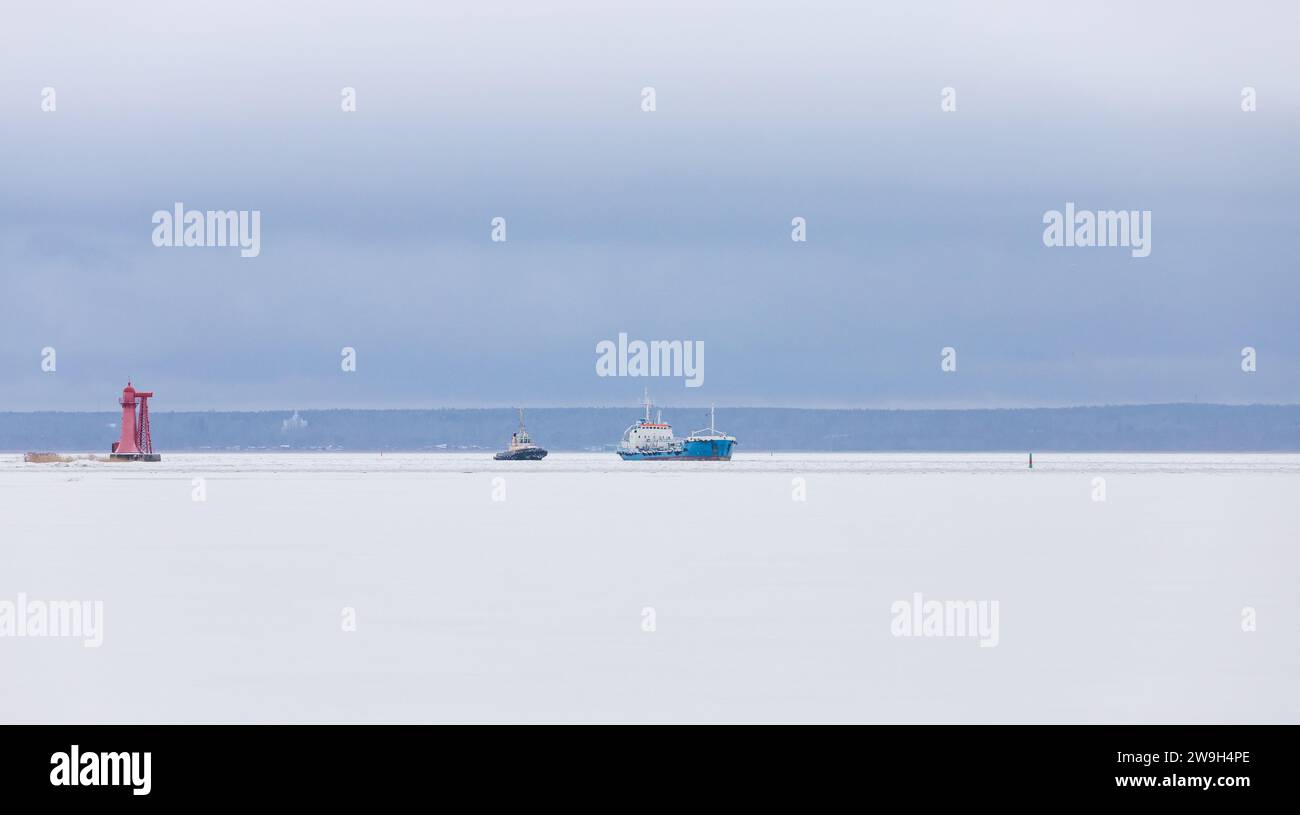 Frachtschiff und Schlepper segeln den Kanal an einem Wintertag, Eisnavigation Stockfoto