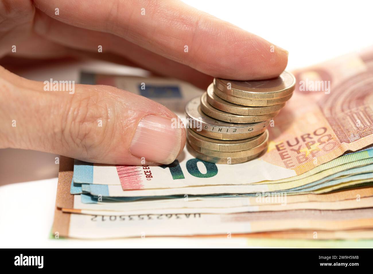 Nahaufnahme mehrerer übereinander gestapelter Euro-Banknoten. Eine Hand greift nach ein paar Münzen, die auf dem Geld liegen. Stockfoto