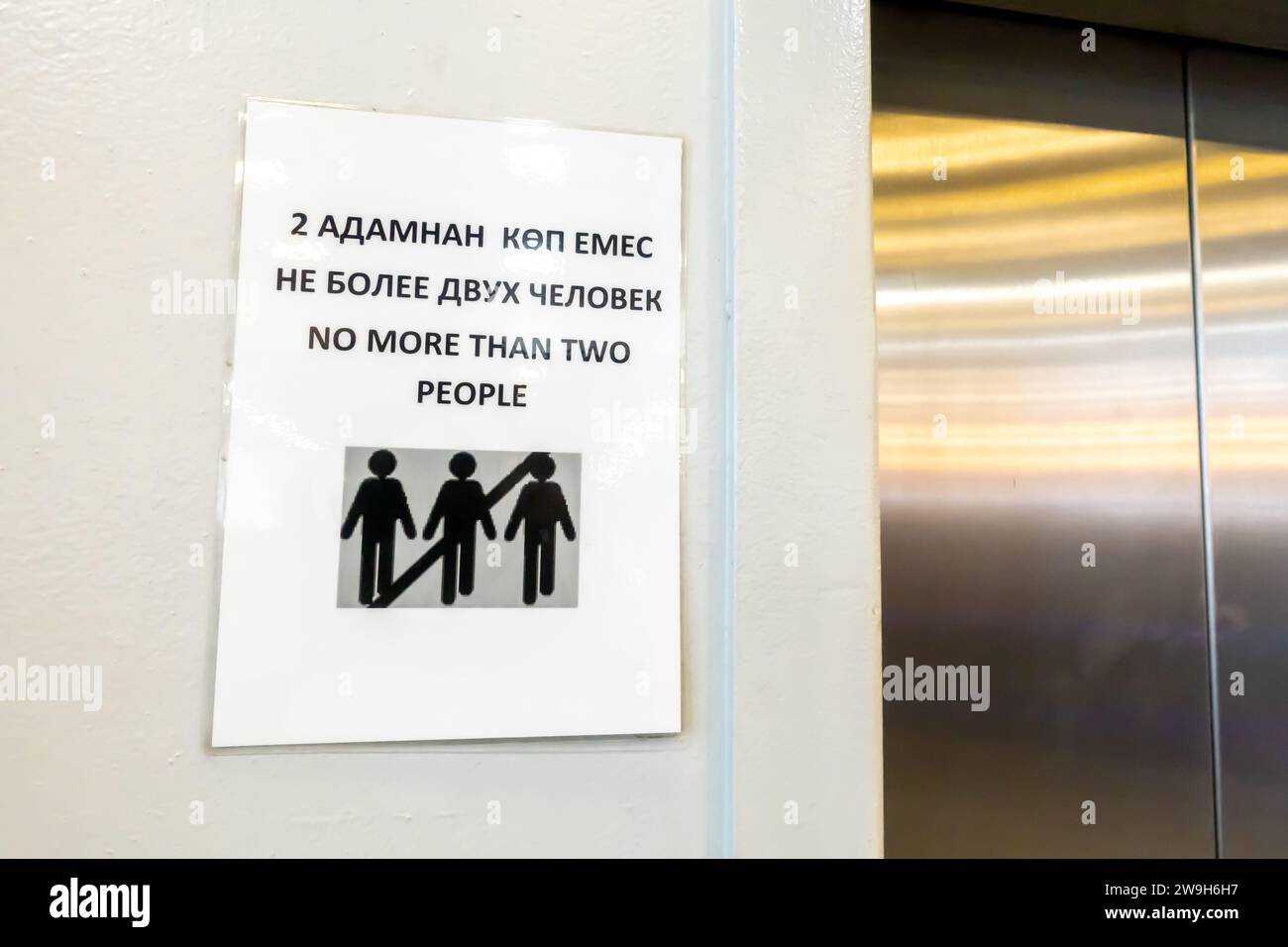 "Nicht mehr als zwei Leute" lächerliches Zeichen, das mehr als zwei Personen in einem Aufzug verbietet. Flughafen Almaty. Lustige Schilder, verboten. Stockfoto