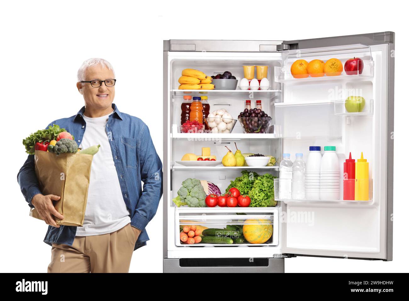 Reifer Mann posiert neben einem offenen Kühlschrank und hält eine Einkaufstasche isoliert auf weißem Hintergrund Stockfoto