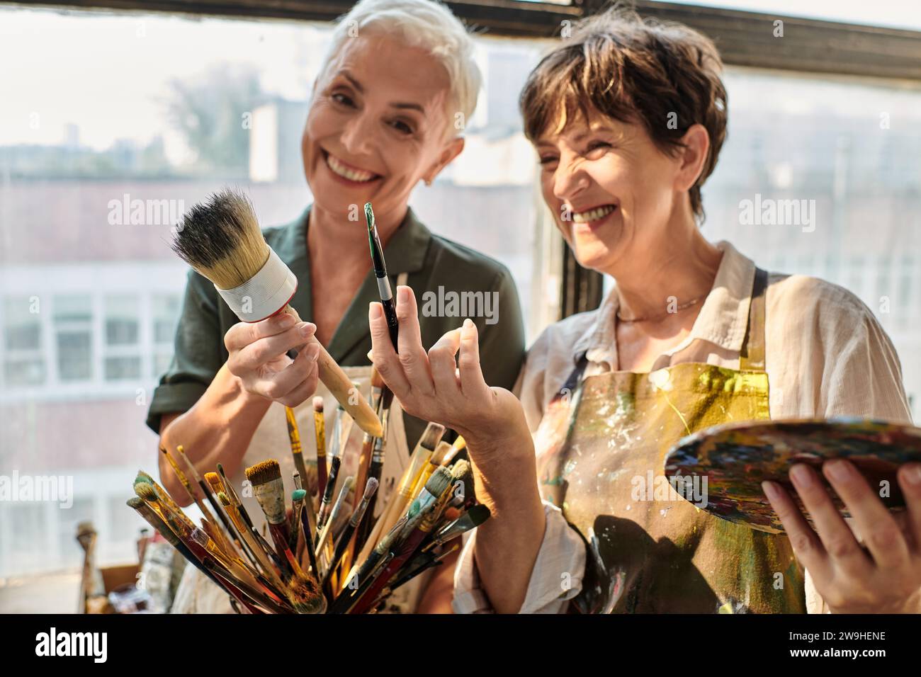 Fröhliche reife Frauen mit verschiedenen Pinseln während des Meisterkurses im Kunststudio Stockfoto