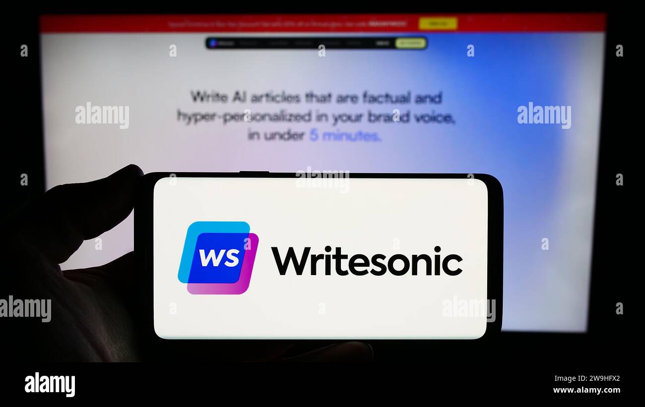 Person, die ein Smartphone mit dem Logo des US-amerikanischen Unternehmens für künstliche Intelligenz Writesonic Inc. Vor der Website hält. Schwerpunkt auf dem Display des Telefons. Stockfoto