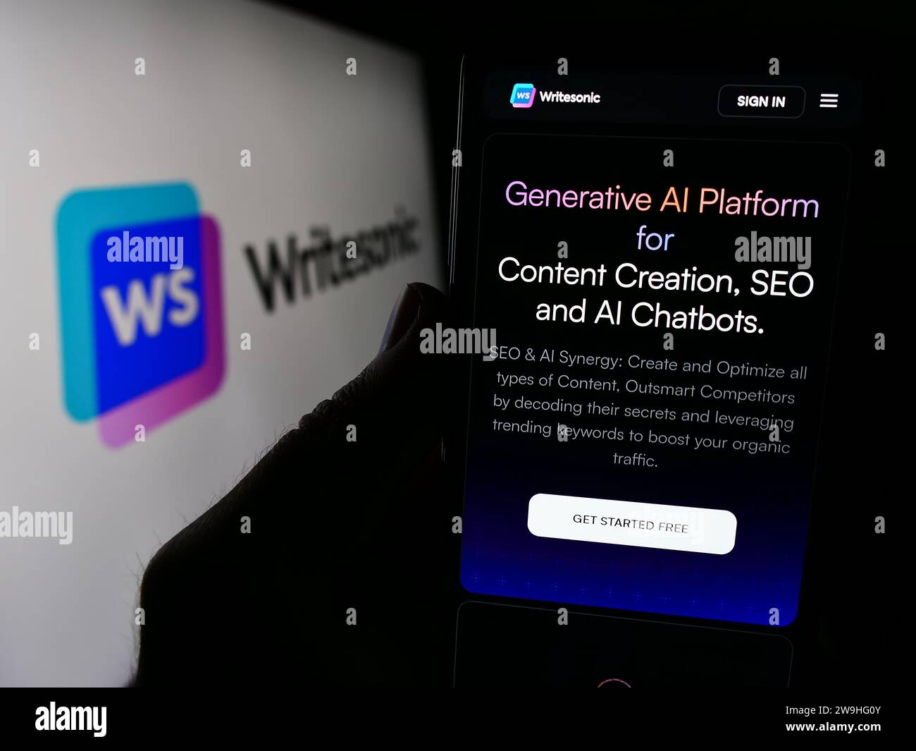 Person, die ein Handy hält, mit Webseite des US-amerikanischen Unternehmens für künstliche Intelligenz Writesonic Inc. Vor dem Logo. Konzentrieren Sie sich auf die Mitte des Telefondisplays. Stockfoto