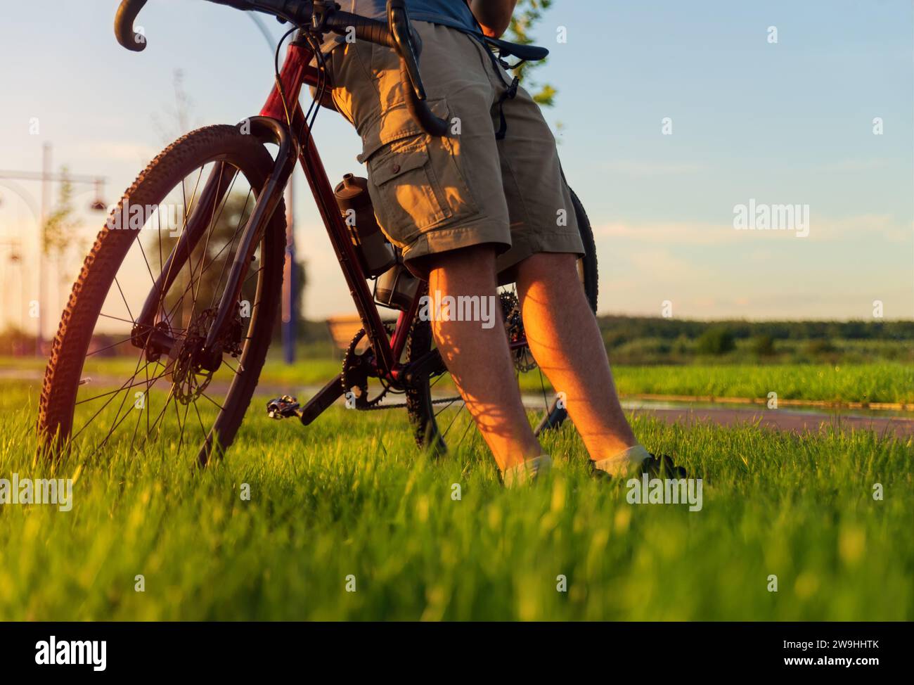 Der Radfahrer sitzt auf einem Schotterrad und liegt auf dem Rasen. Radfahren durch den Park an einem Sommerabend bei Sonnenuntergang. Aktives Lifestyle-Konzept. Stockfoto
