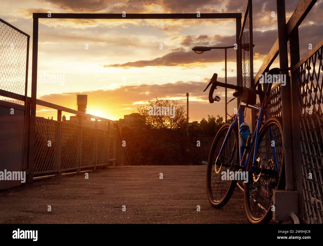 Ein Rennrad steht in der Nähe des Zauns. Fahrradsilhouette auf dem Himmelhintergrund bei Sonnenuntergang. Wunderschöne Landschaft. Stockfoto
