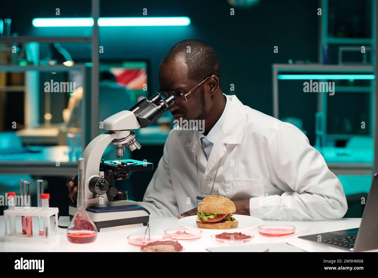 Professioneller afroamerikanischer Forscher, der künstliches Fleisch durch das Mikroskop betrachtet Stockfoto