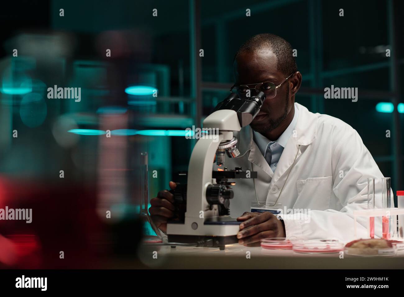 afroamerikanischer Wissenschaftler sitzt am Arbeitsplatz im Labor und arbeitet mit Mikroskop Stockfoto