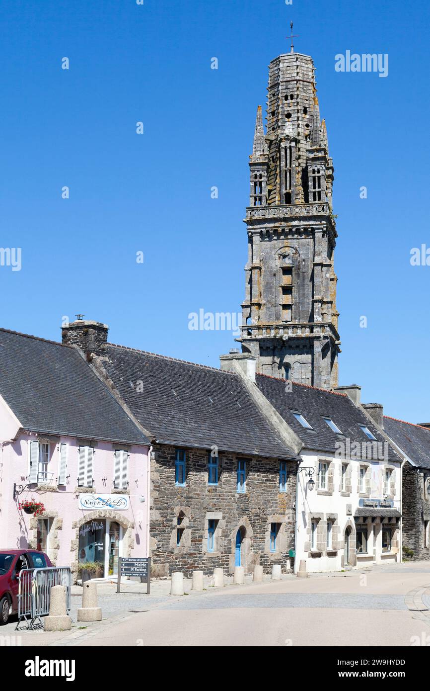 Lampaul-Guimiliau, Frankreich - 09. Juli 2022: Die Kirche Notre-Dame mit ihrem getürmten Glockenturm mit Blick auf die Häuser der Stadt. Stockfoto
