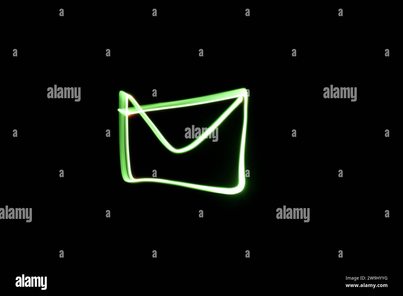 Ein Foto einer Post oder eines Umschlagsymbols in leuchtendem grünem Licht in einem Langzeitfoto vor schwarzem Hintergrund. Lichtmalerei Stockfoto