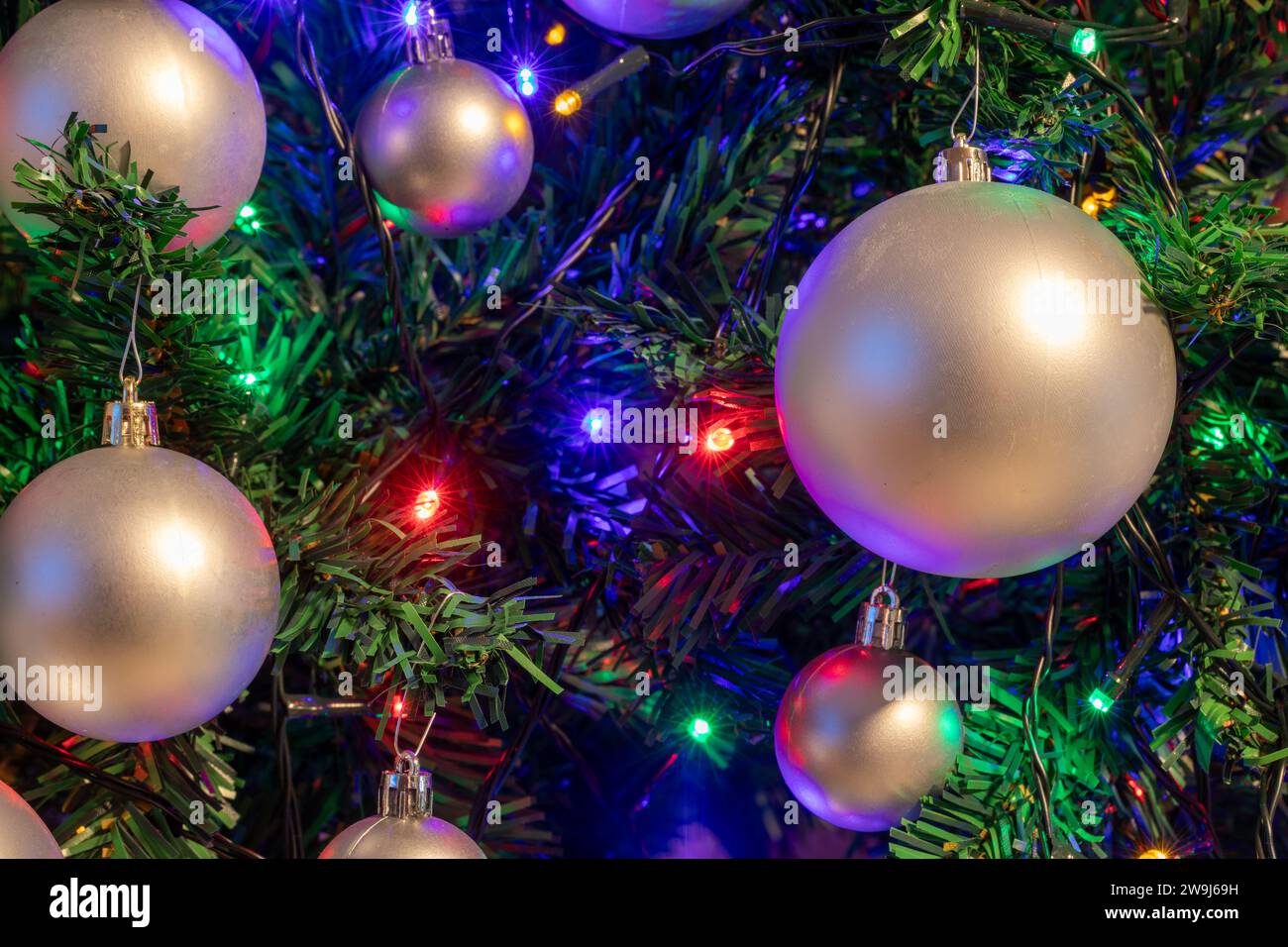 Künstlicher Weihnachtsbaum mit Ornamenten und Lichtern - Feiertagshintergrund und Textur Stockfoto