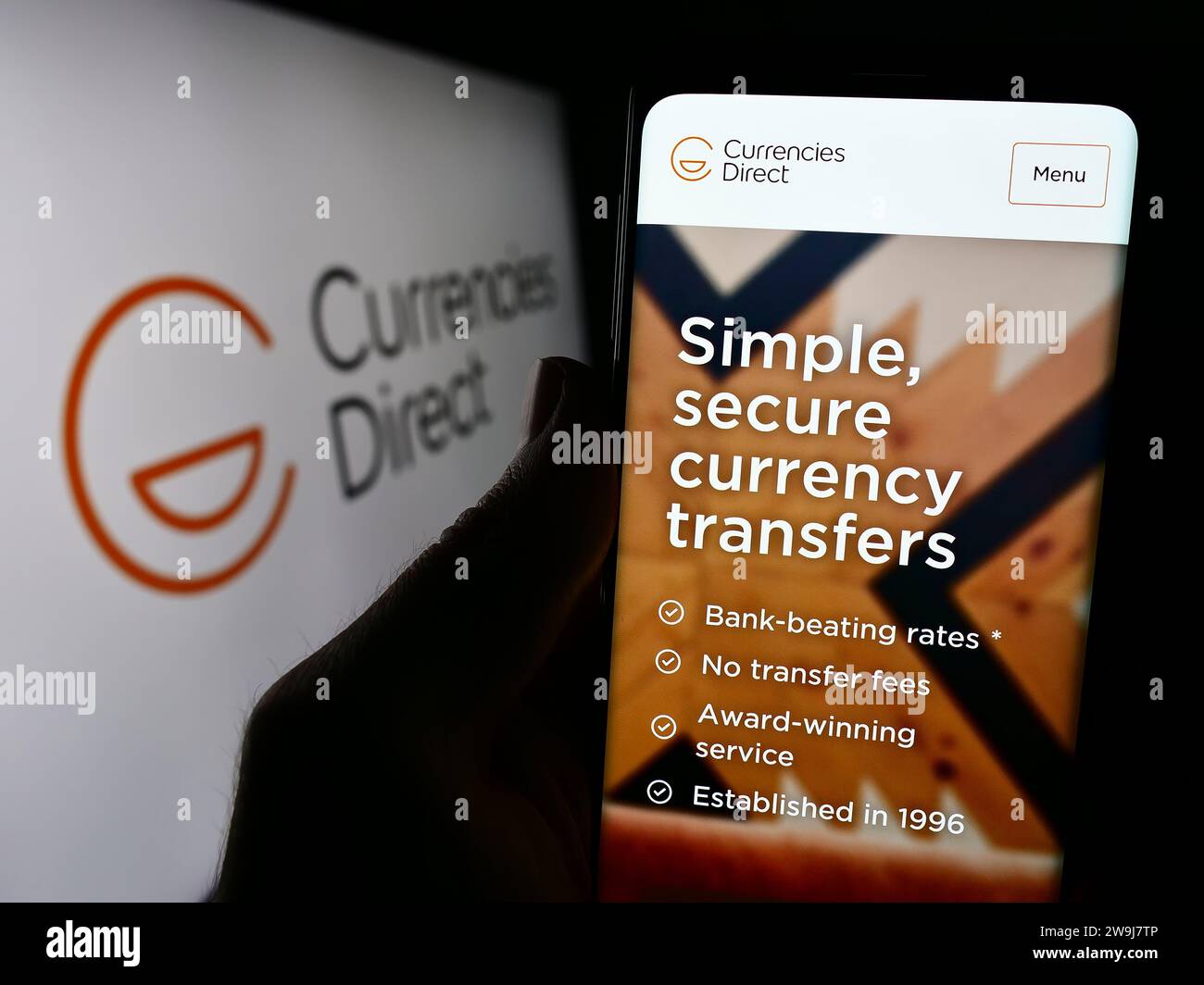 Person, die ein Handy hält, mit Webseite der britischen Geldtransfergesellschaft Currency Direct Ltd. Vor dem Logo. Konzentrieren Sie sich auf die Mitte des Telefondisplays. Stockfoto