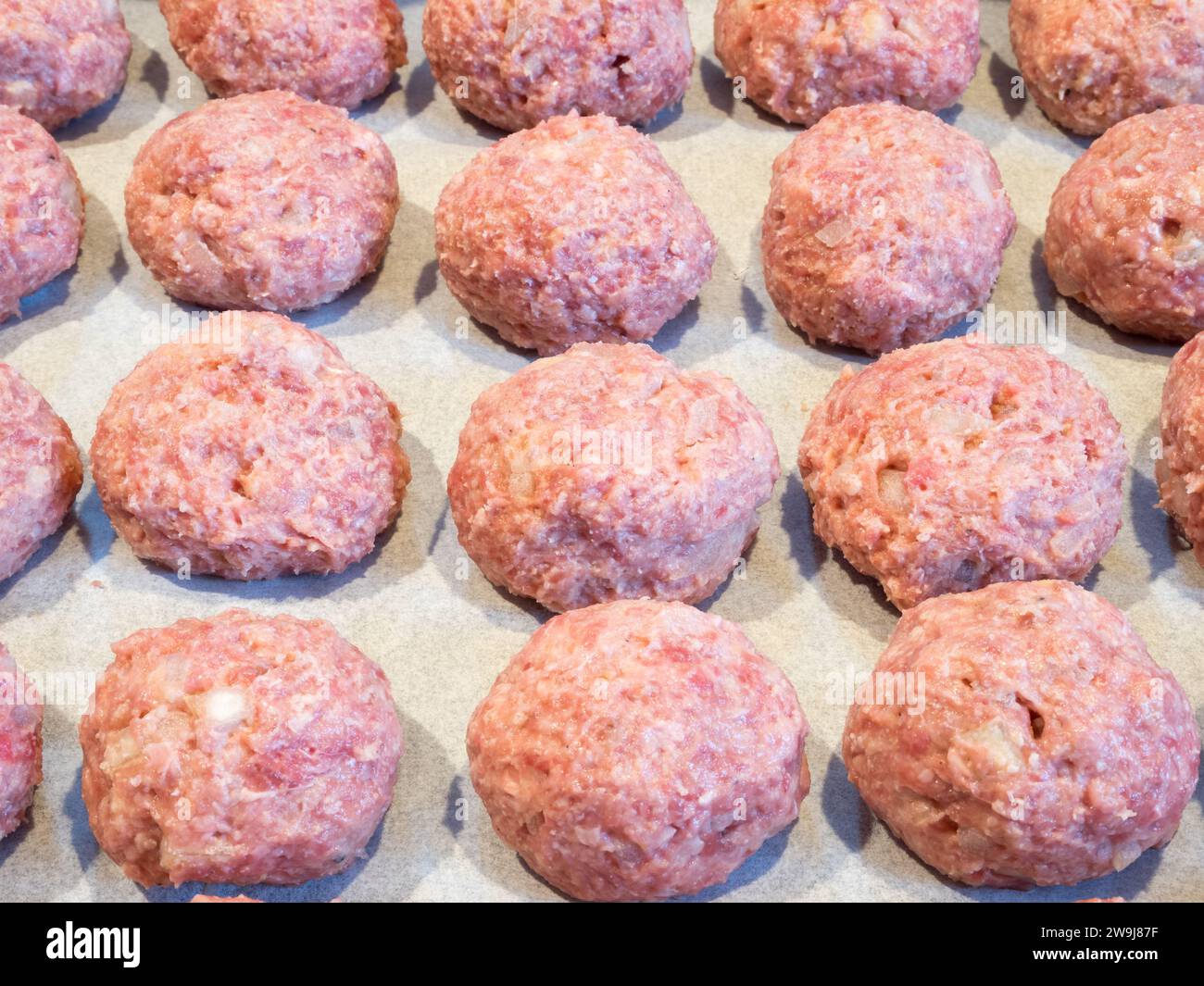 Köstliche Fleischbällchen, ordentlich auf einem mit Pergamentpapier ausgelegten Blech angeordnet, bereit für den ersten Backofen vor dem Frittieren. Stockfoto