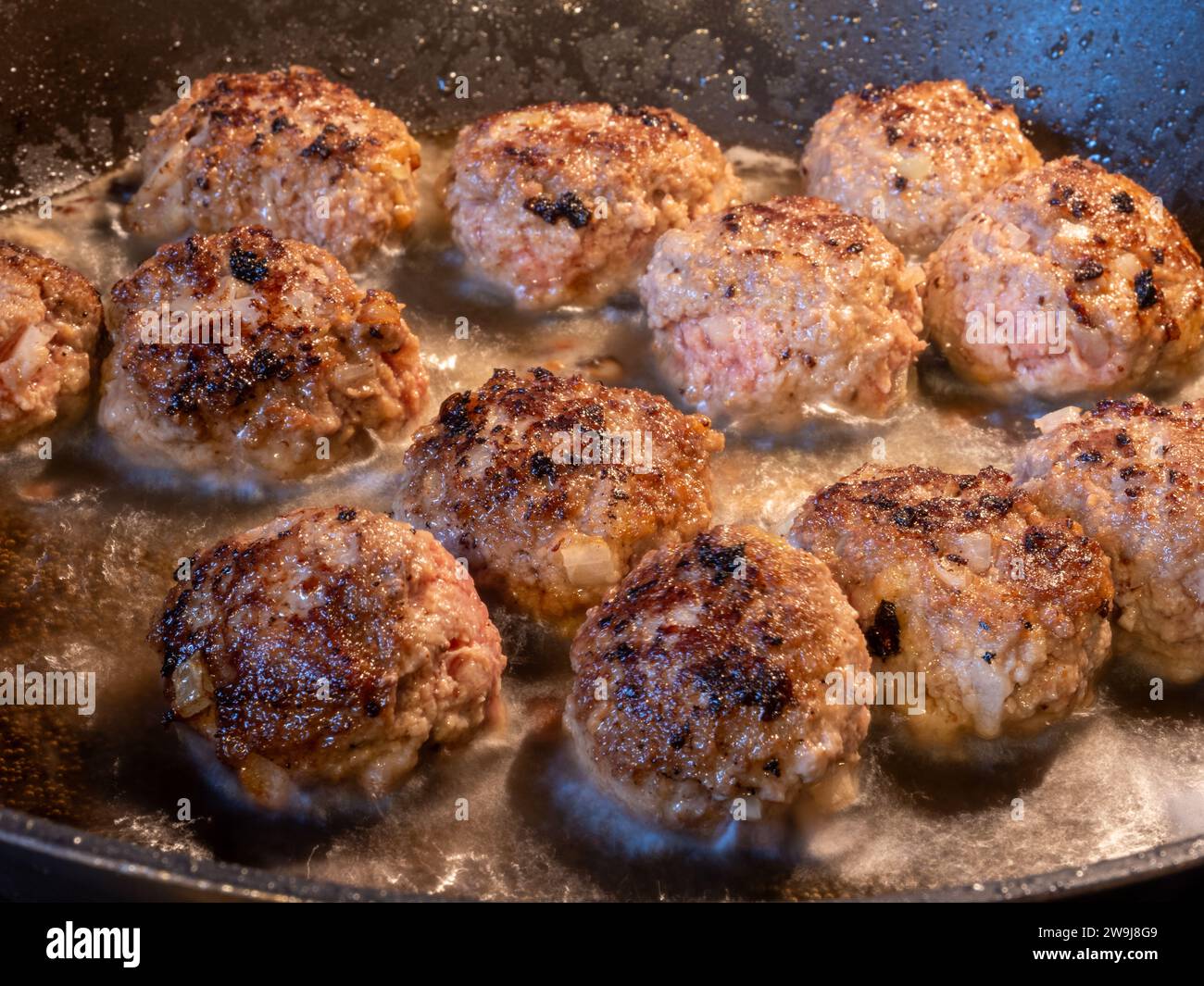 Eine fokussierte Perspektive, in der brausende goldbraune Fleischbällchen in sprudelnder Butter in einer Pfanne festgehalten werden. Stockfoto