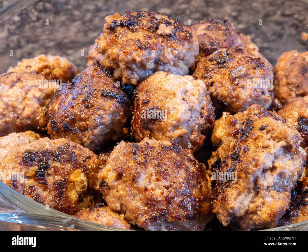 Glänzende goldbraune Fleischbällchen schmücken eine Glasschale, die auf einer dunklen, polierten Granitplatte steht. Stockfoto