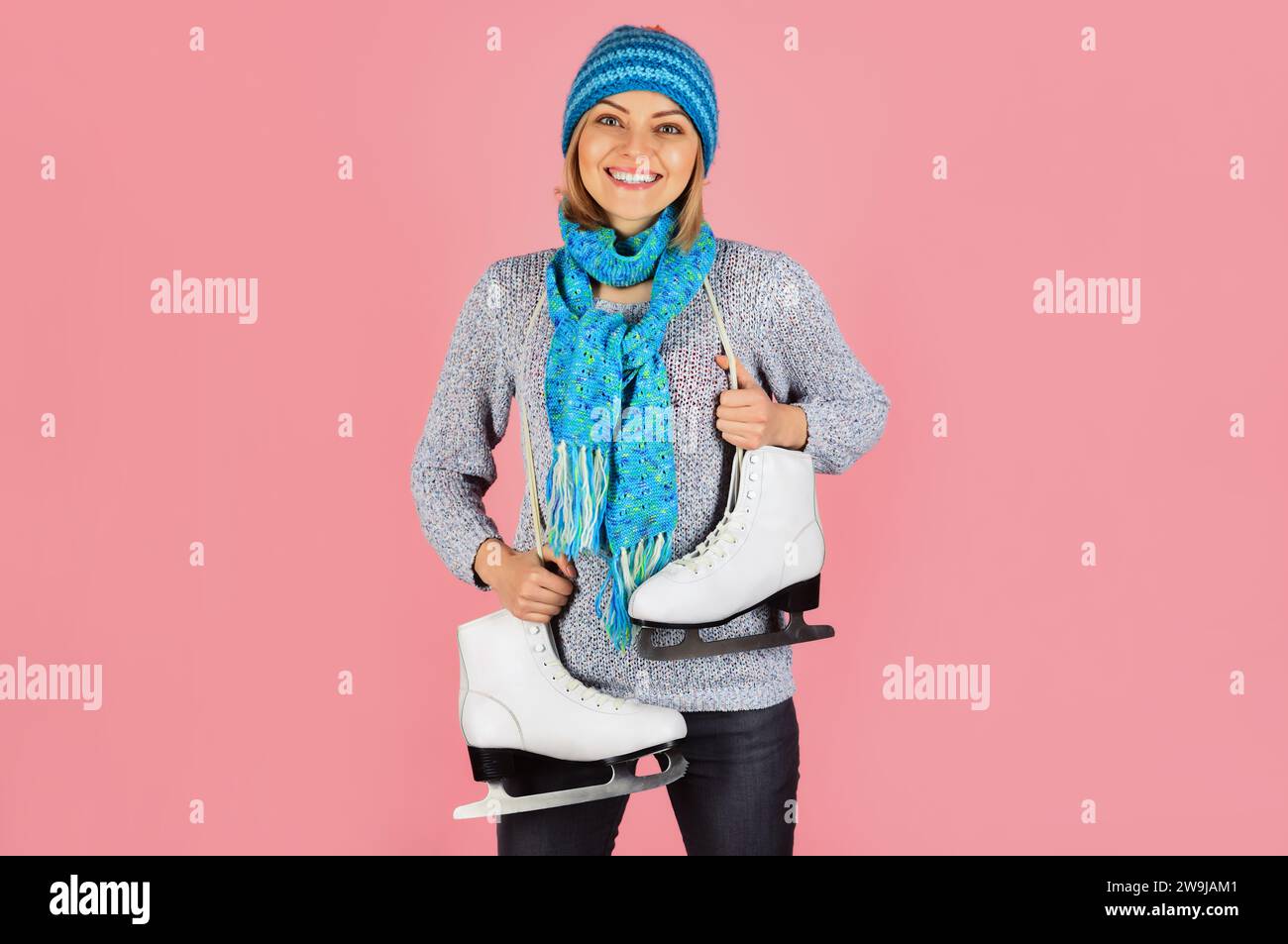Lächelndes Mädchen in Strickpullover, Schal und Hut mit Schlittschuhen. Wintersportaktivitäten. Hübsche Frau in warmer Kleidung mit Schlittschuhen, die bereit sind Stockfoto