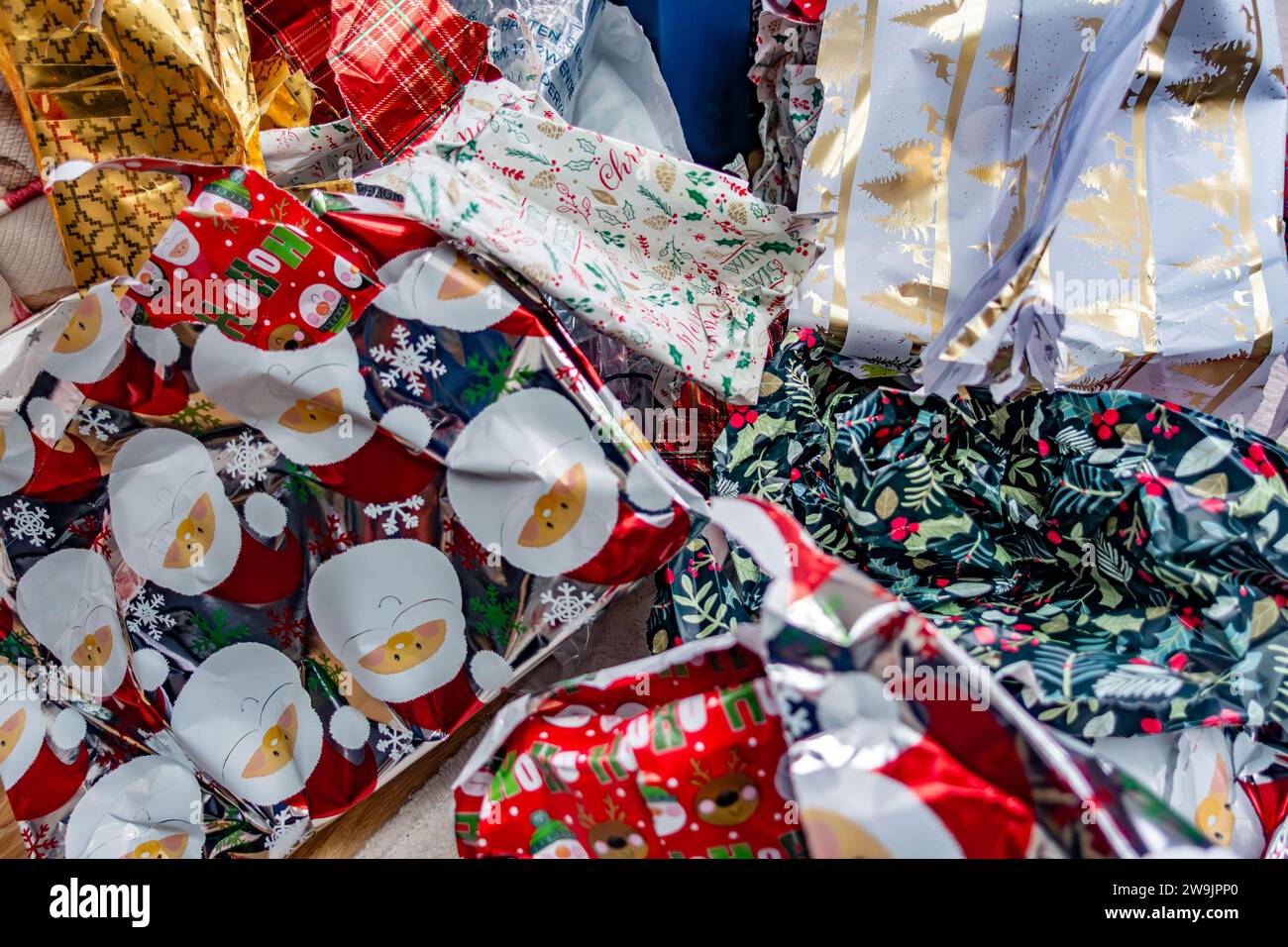 Weggeworfenes Weihnachtspapier, das auf einem Stapel auf dem Boden liegt, wurde von Weihnachtsgeschenken abgerissen Stockfoto