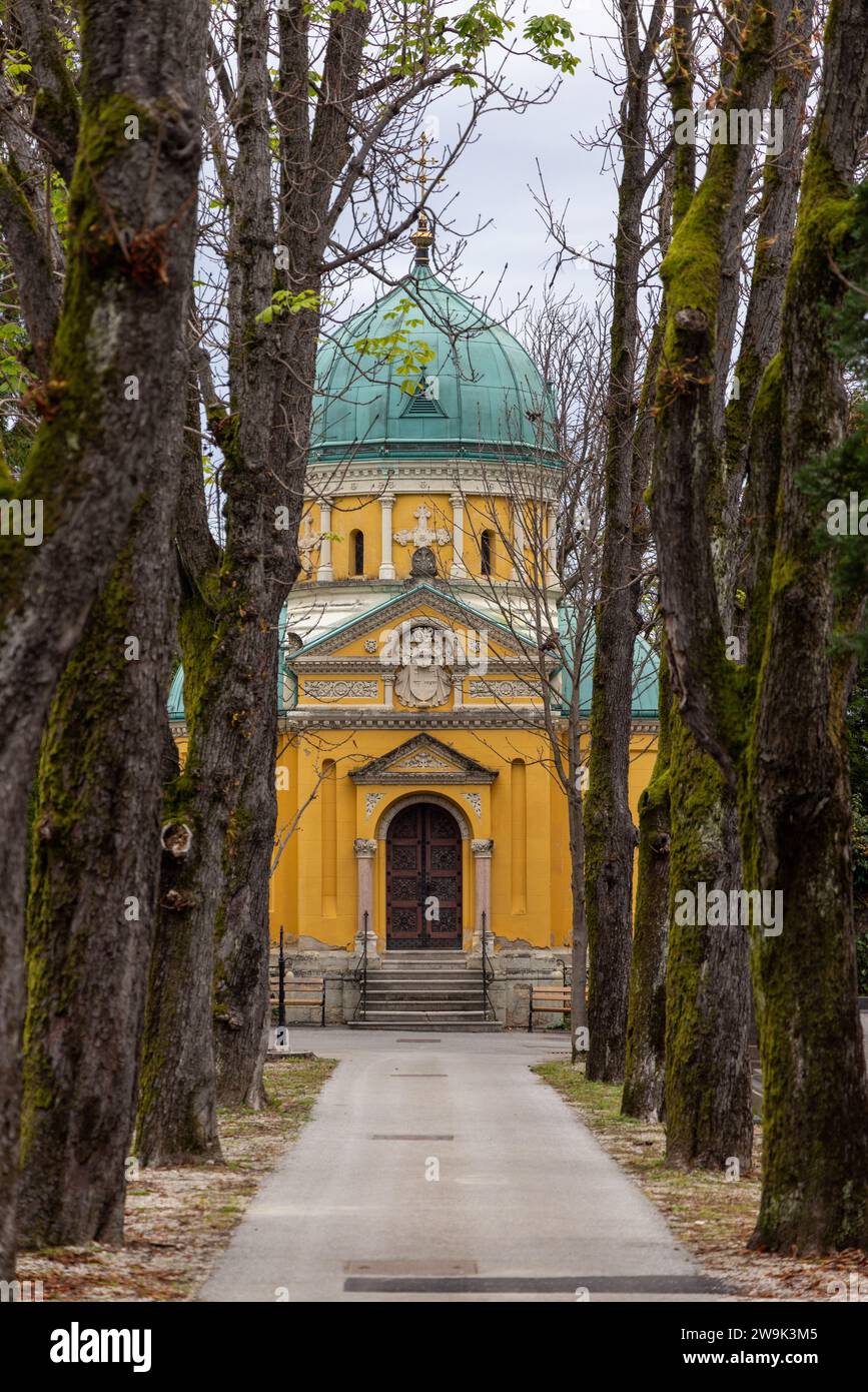 Von Bäumen gesäumte Gasse in Richtung des gelben Gebäudes der orthodoxen Kapelle der heiligen Apostel Peter und Paul auf dem Mirogoj-Friedhof in Zagreb, Kroatien Stockfoto
