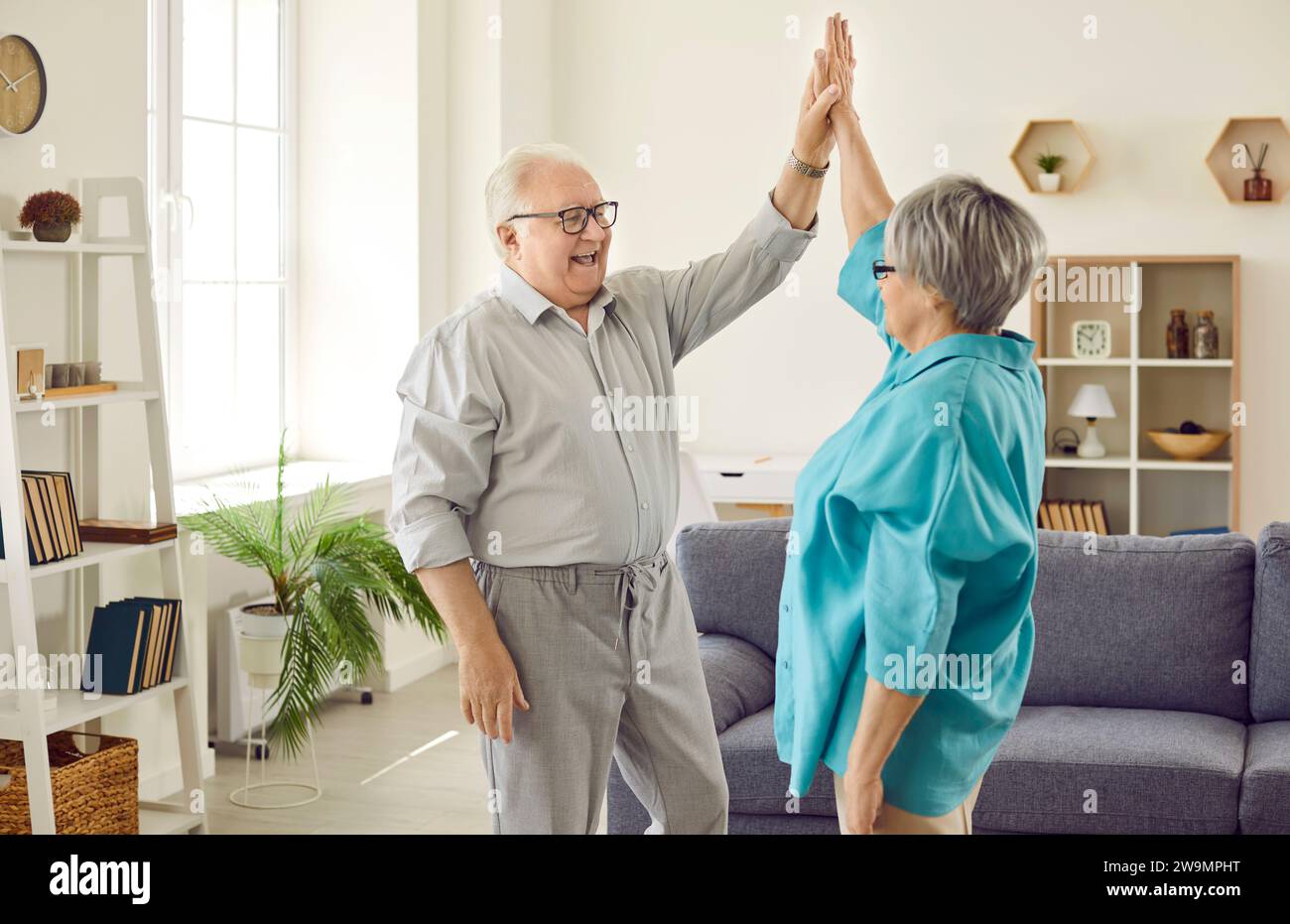 Seniorenpaar, das zu Hause steht und sich gegenseitig High Five gibt, um Erfolg zu feiern Stockfoto