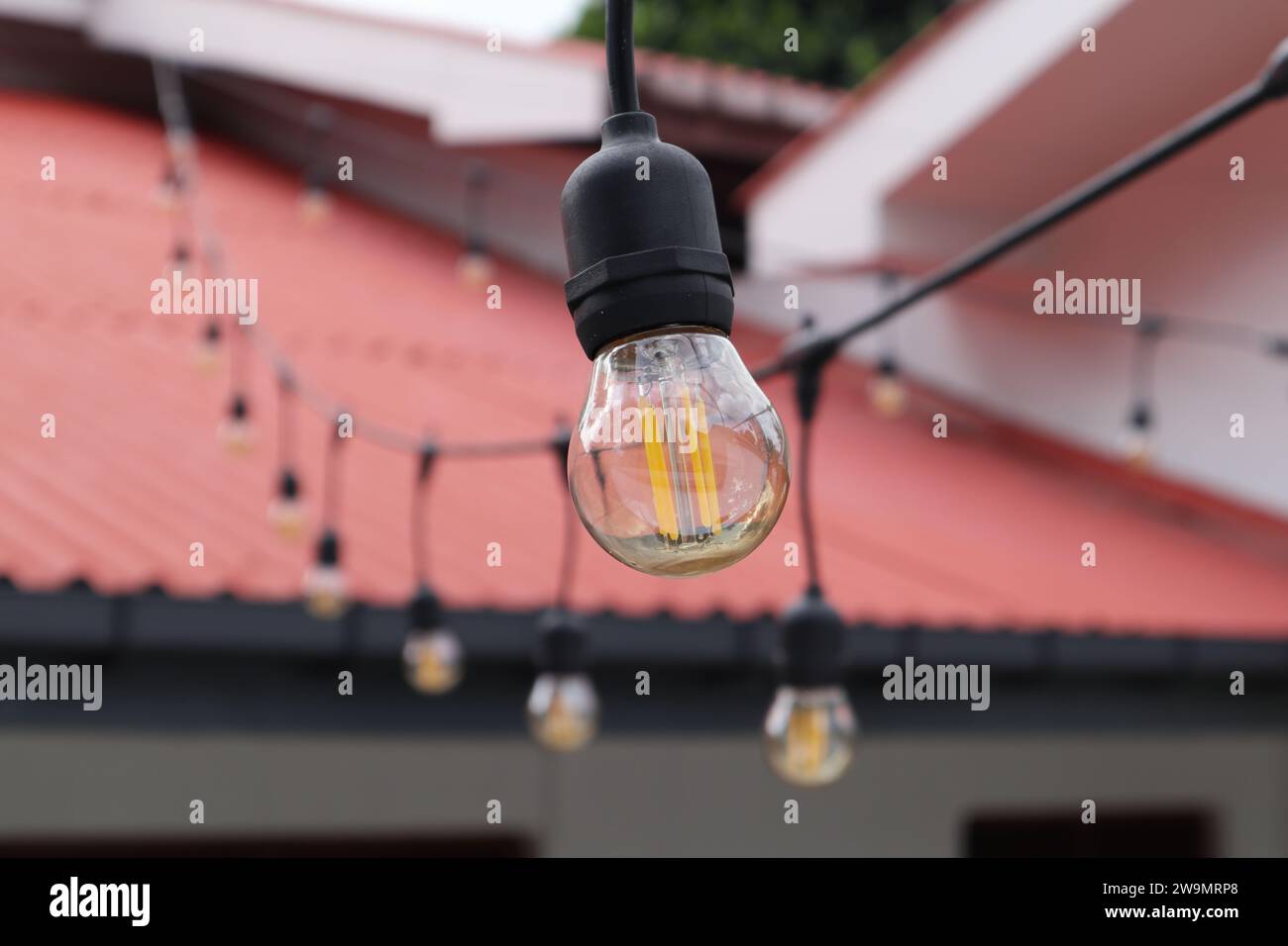 Eine kleine kugelförmige LED-Lampe im Edison-Stil mit orangefarbenen Filamenten und klarem braunem Glas. Dies ist eine Außendekoration Strang Lampe Stockfoto