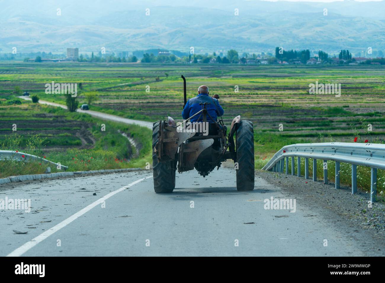 Alter Mann, der Traktor fährt, auf der Straße. Querformat. Auf Dem Land. Landschaft. 5. 8. 2023 Sokolarci. Mazedonien Stockfoto