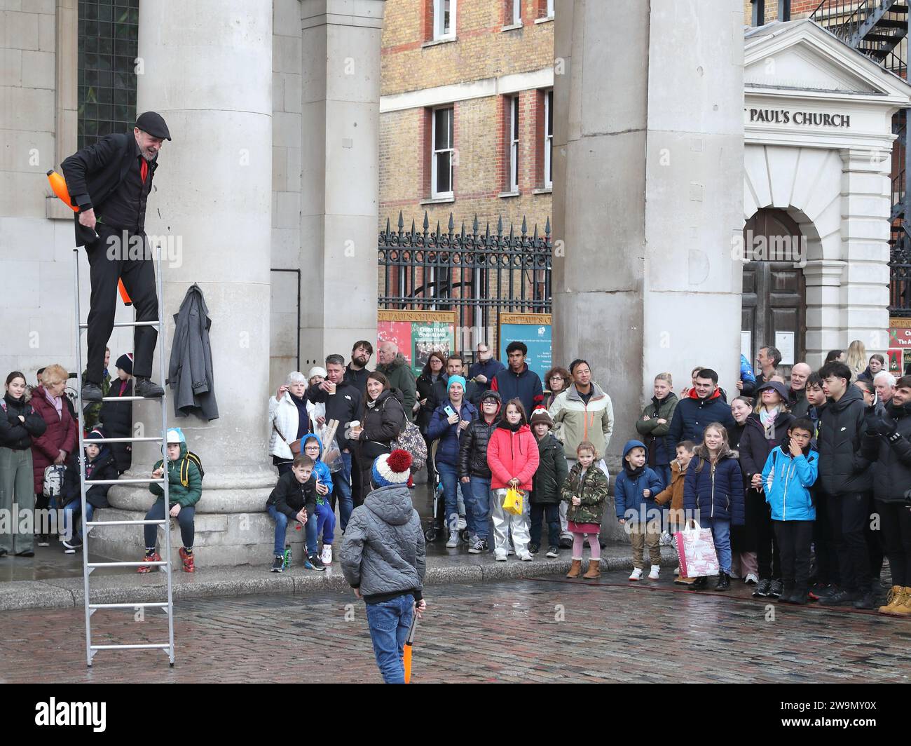 An einem regnerischen Tag unterhält ein Straßenkünstler auf einer Leiter die Zuschauer in Covent Garden, London, Großbritannien Stockfoto