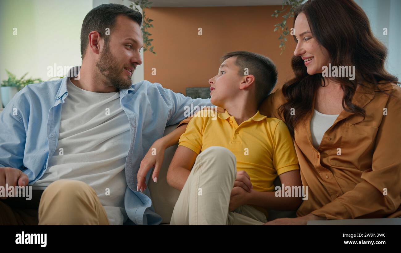 Glückliche kaukasische Familie, die sich am Wochenende zu Hause entspannt, liebevolle Eltern, Mama, Dad, spricht mit Sohn, Kind, das sich auf einer gemütlichen Couch umarmt Stockfoto