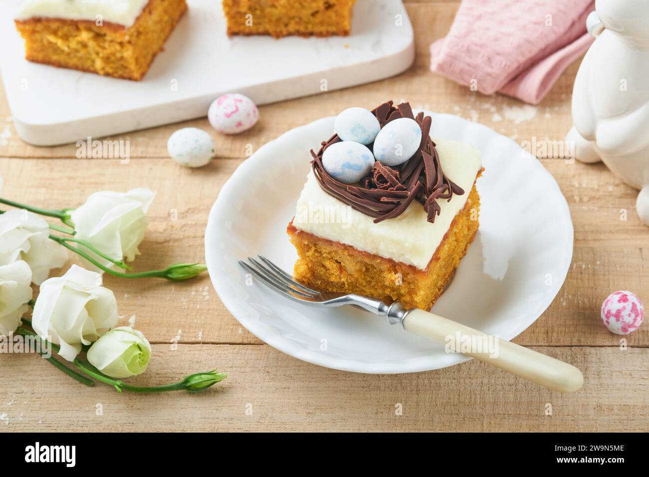 Osterkuchen mit Schokoladennest und Schokoladeneiern, blühende Kirsch- oder Apfelblüten auf rustikalem hellem Holzhintergrund. Stockfoto