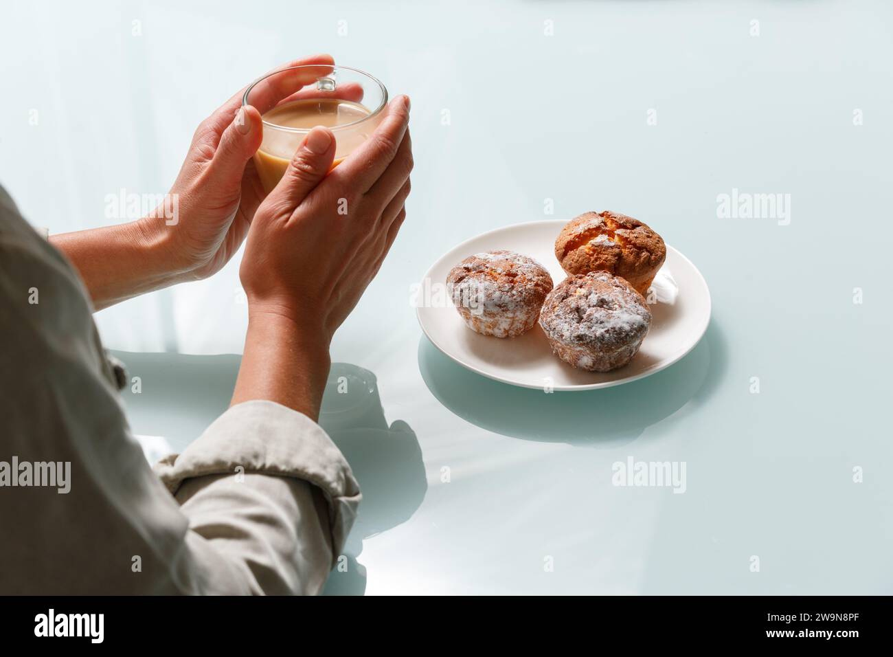 Nahaufnahme der Hände, die eine Tasse Kaffee mit Milch und drei Quark-Muffins auf dem Teller auf der rechten Seite halten. Köstlicher und aromatischer Snack Stockfoto