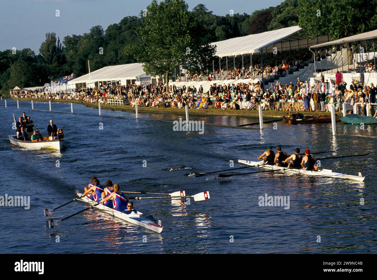 Sommer England Ruderregatta UK. Henley Royal Regatta. Die Siegersportler beobachten das Ruderrennen vom Ufer der Tribüne aus. Das Judges Boat folgt den beiden Mannschaftsbooten, während sie die Ziellinie überqueren. Henley on Thames, Oxfordshire, Juli 1995 1990, UK HOMER SYKES Stockfoto