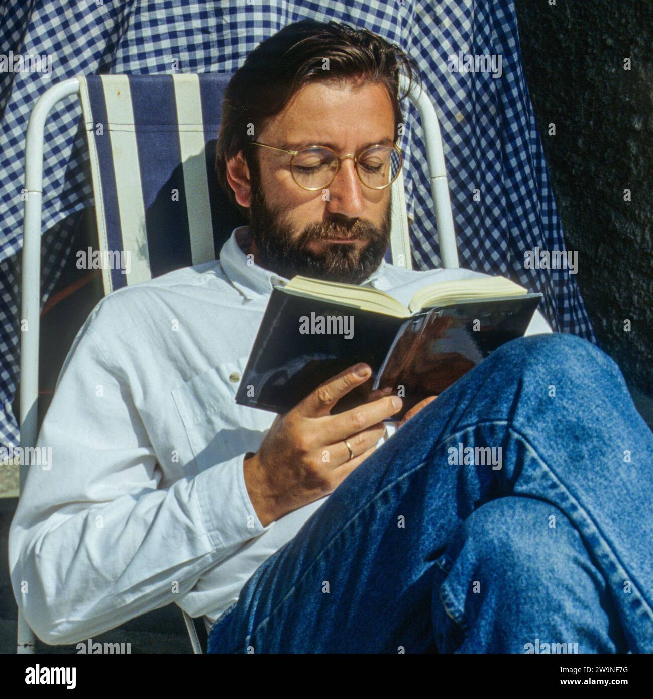 Ein Mann liest ein Buch. Der bärtige Mann sitzt auf einem Stuhl und liest ein Buch. Stockfoto