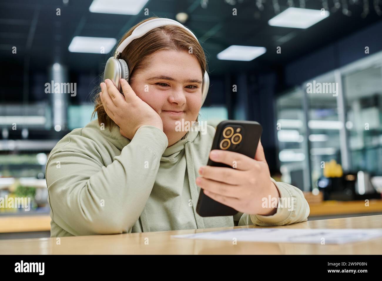Fröhliche Frau mit psychischen Störungen, die Smartphone hält und Musik im Kopfhörer im Café hört Stockfoto