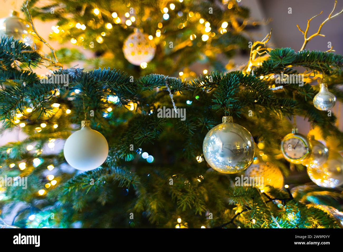 Hängende Ornamente erleuchten einen Weihnachtsbaum, umgeben von dem sanften Leuchten verschwommener Weihnachtslichter. Stockfoto