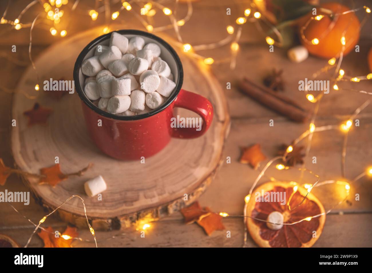 Niedliche, gemütliche Winterkomposition. Rote Tasse, Marshmallows, Orangen und Weihnachtslichter. Silvester und weihnachten, Wärme, Komfort Stockfoto