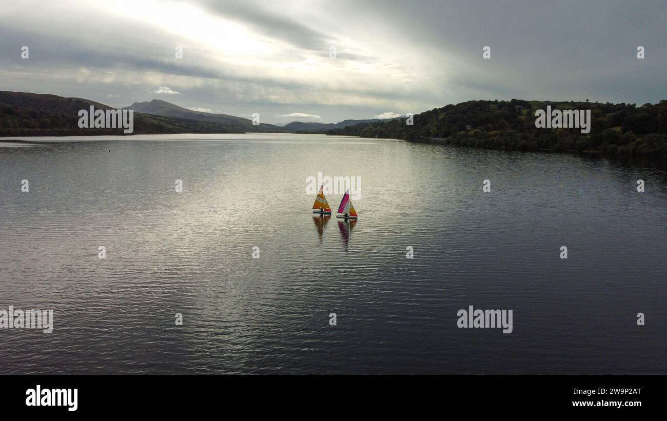 Segeln unter bewölktem Himmel auf Lake Bala, Wales. Gestreifte Segel in leuchtenden Farben sorgen für einen ruhigen Kontrast vor der bergigen Kulisse. Stockfoto