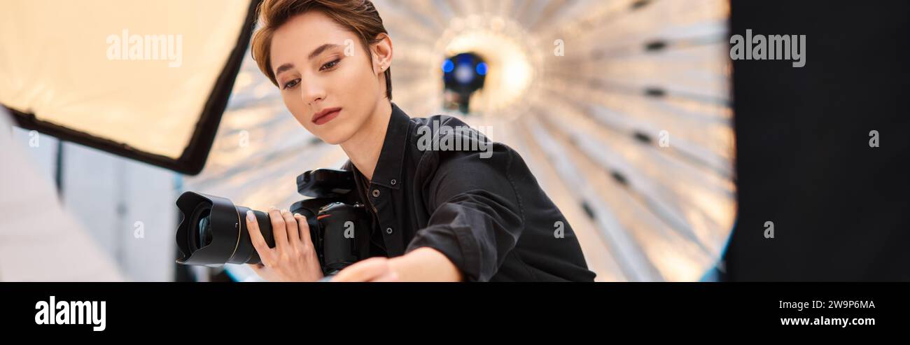 Eine attraktive fokussierte Fotografin, die eine Kamera hält und sich darauf vorbereitet, Fotos in ihrem Studio zu machen Stockfoto