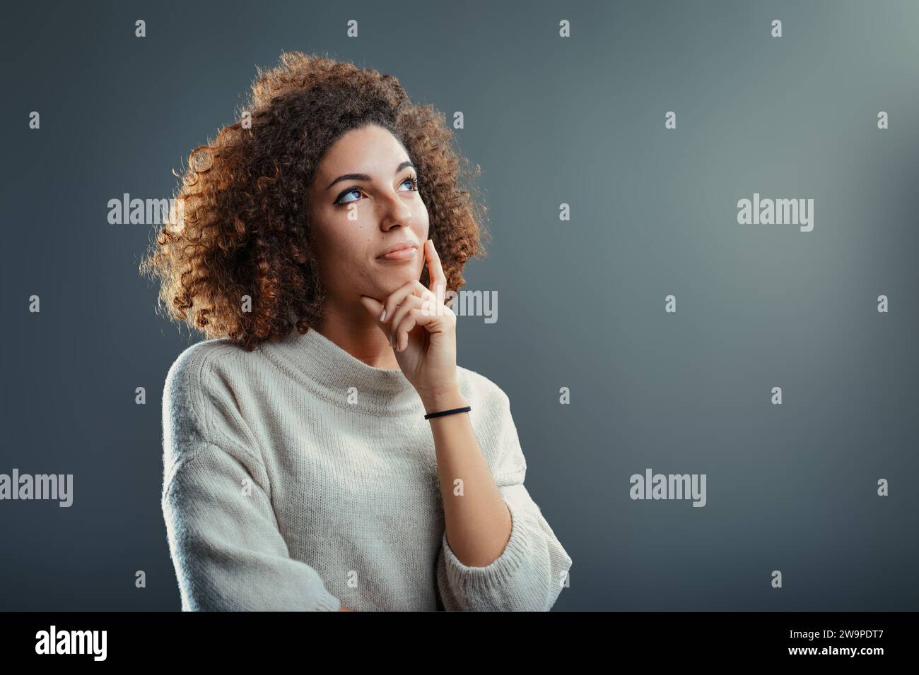 Ein nachdenklicher Ausdruck inmitten einer ruhigen, nachdenklichen Frau mit lockigen Haaren scheint in der Besinnung verloren zu sein, ihr Blick erhob sich in Reflexion nach oben Stockfoto