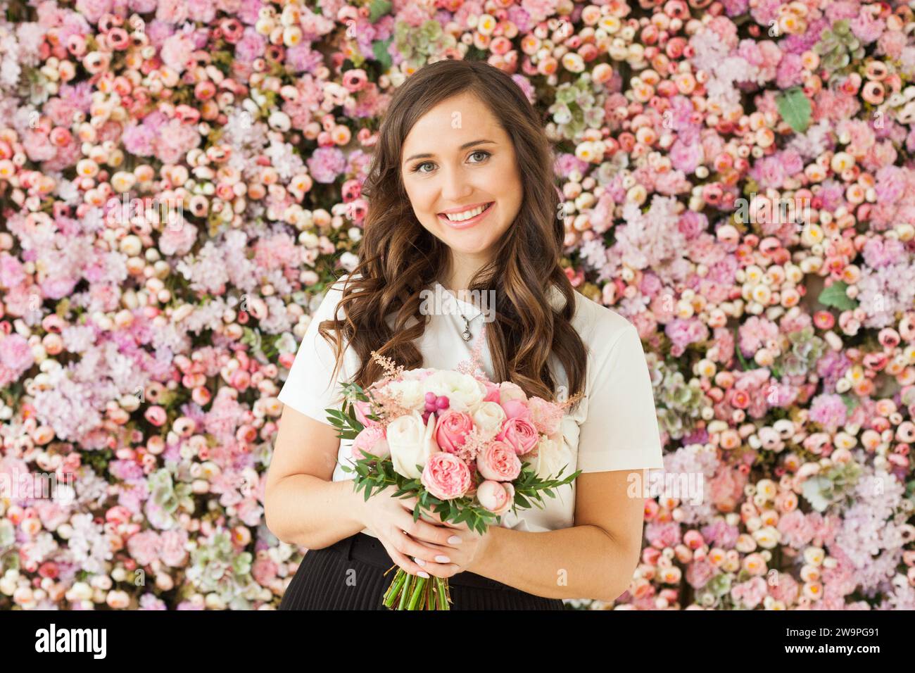 Frühlingsportrait einer glücklichen brünetten Frau mit niedlichem Lächeln, das Blumengeschenk hält und auf rosa floralem Hintergrund posiert. Blooming, Liebe, 8. märz Geburtstag, ho Stockfoto