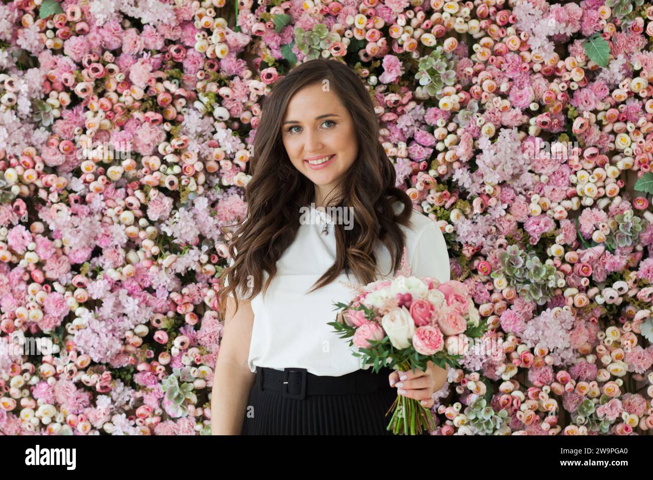 Attraktive glückliche brünette Frau mit niedlichem Lächeln, die Blumengeschenk hält und auf rosa floralem Hintergrund posiert. Blooming, Liebe, Geburtstag am 8. märz Stockfoto