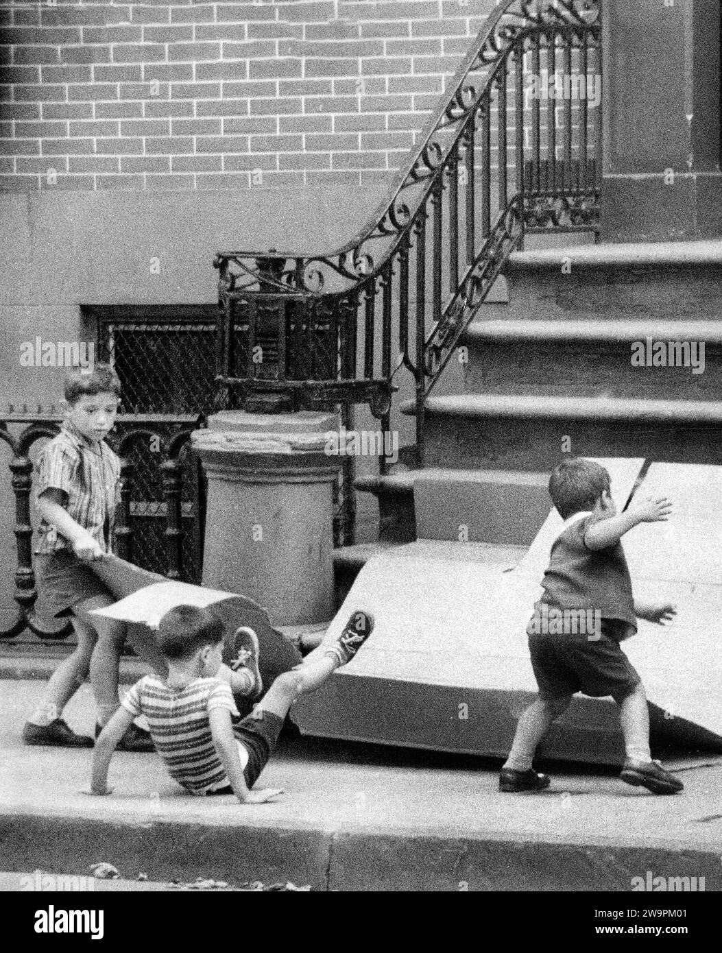 Drei kleine Jungs, die Pappe benutzen, um die vorderen Stufen des Wohngebäudes herunterzugleiten, New York City, New York, USA, Angelo Rizzuto, Anthony Angel Collection, August 1956 Stockfoto