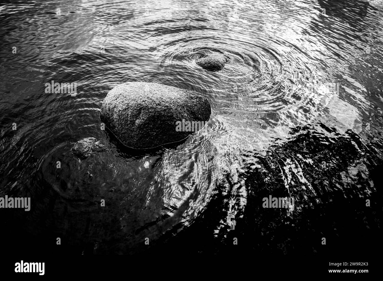 Wellen Sie Muster um Felsen in einer ruhigen Wasseroberfläche. Stockfoto