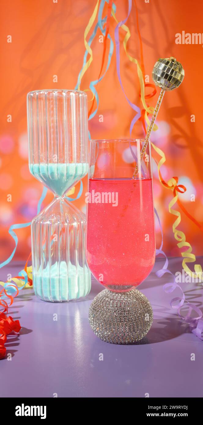 Ein Sandtimer Countdown und ein Glas Pink Celebration mit glitzerndem Champagner mit Partyströmen und Konfetti, NeujahrsCountdown Stockfoto
