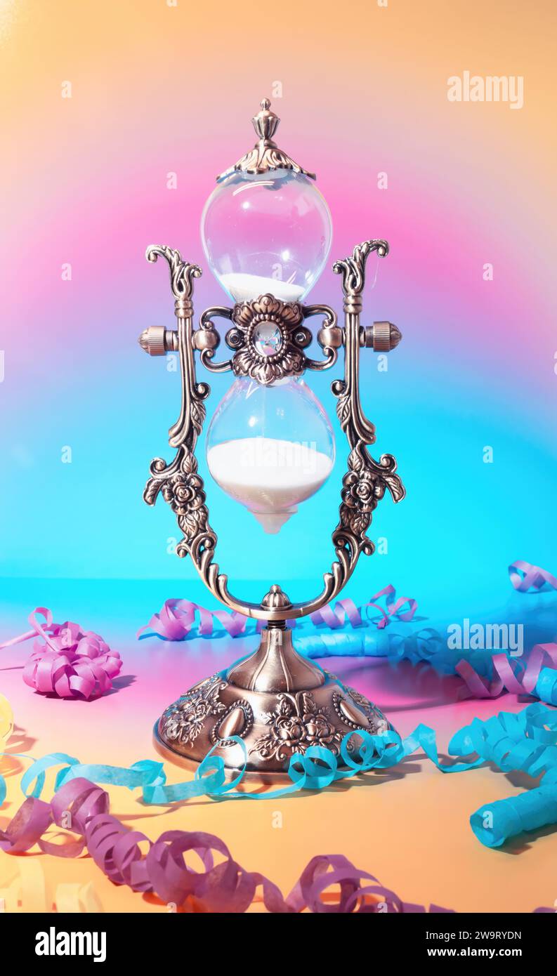 Ein viktorianischer Sand Timer Countdown mit Party Streamers in dekoriertem Celebration Event auf einem pastellrosa und blauen Farbverlauf Hintergrund Stockfoto