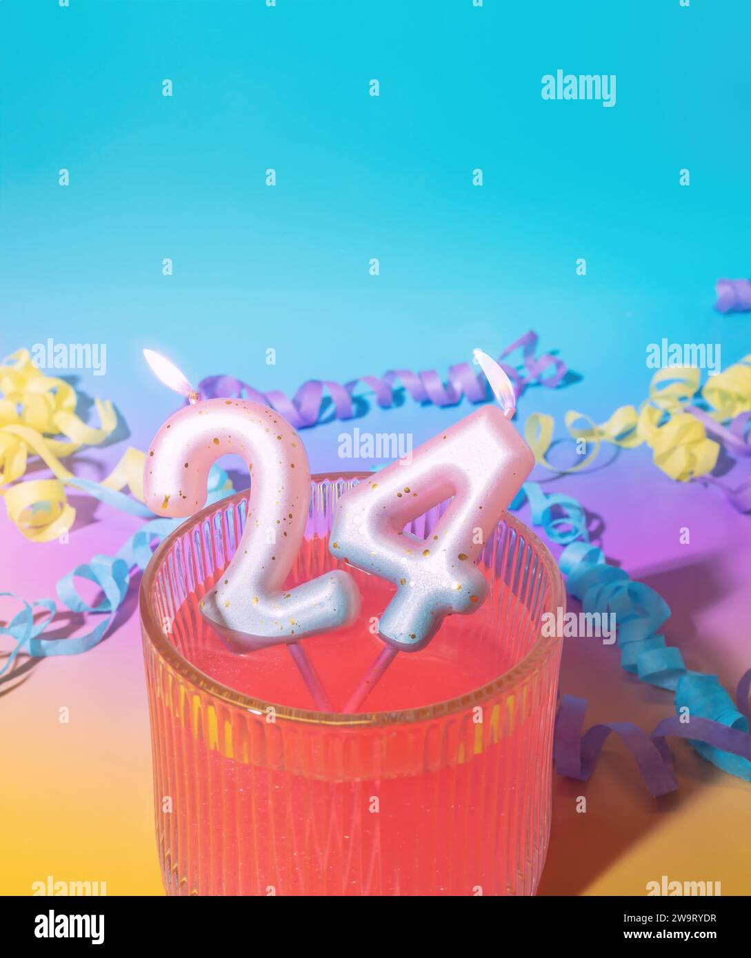 24. Geburtstagsfeier flammende Geburtstagskerzen in einem Cocktailglas und Party-Streamer auf einem Pastellverlauf Hintergrund, Geburtstagsfeier, 24. Jahrestag Stockfoto