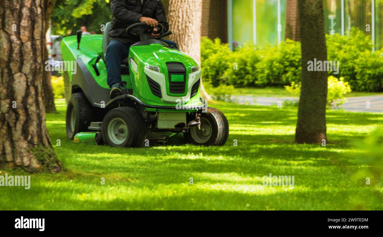 Professioneller Mitarbeiter, der grünes Gras mit einem Rasenmäher-Traktor im Park mäht. Rasenpflegekonzept. Stockfoto