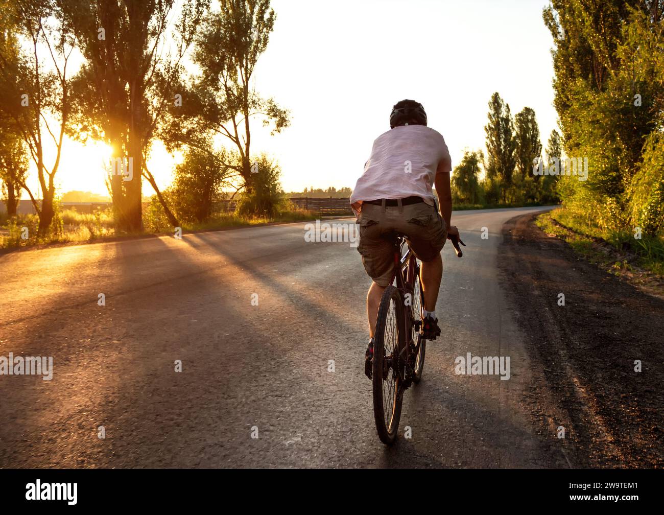 Ein Mann auf einem Rennrad fährt bei Sonnenuntergang eine leere Asphaltstraße. Aktives Lifestyle-Konzept. Stockfoto