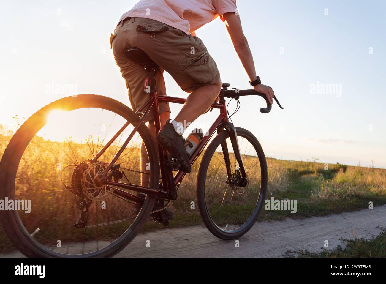 Radfahrer auf dem Feld. Junger Sportmann fährt mit seinem Fahrrad bei Sonnenuntergang mit Sonnenstrahl. Aktives Lifestyle-Konzept. Stockfoto